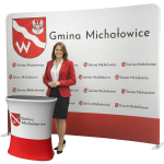 Profesjonalny zestaw wystawienniczy: biała tekstylna ścianka reklamowa z logo Gminy oraz dopasowana trybunka promocyjna