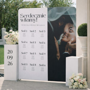 Fotografia w orientacji pionowej prezentuje ściankę z planem stołów weselnych w eleganckiej, jasnej aranżacji plenerowej. Projekt łączy czytelną listę gości z estetycznym układem graficznym i personalizowanym motywem ślubnym.