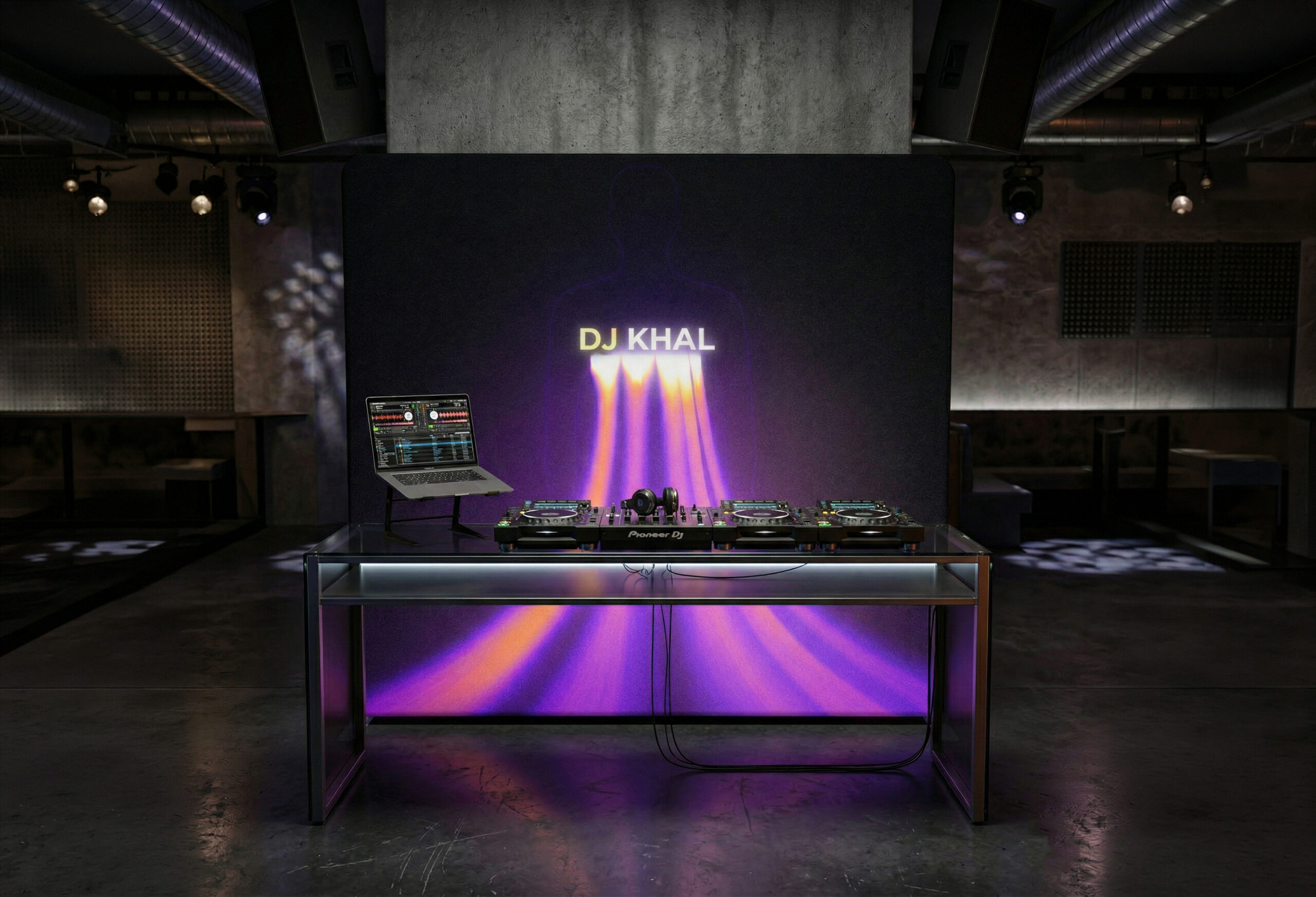 Stanowisko DJ-a z profesjonalną konsolą i laptopem, ustawione na tle nowoczesnej ścianki eventowej z neonowym napisem DJ KHAL i fioletowo-pomarańczowymi promieniami światła w surowym wnętrzu klubu.